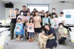 《與動物相愛的練習︱狗狗的家人時光遊戲課》學員與待認養狗狗溫馨合影，手舉認養犬隻的介紹牌。